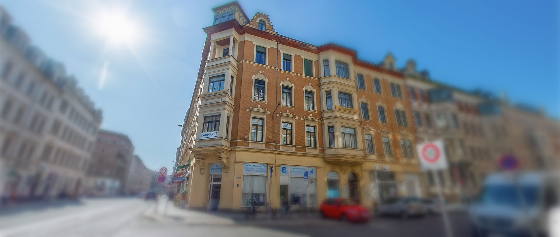 Ein altes, mehrstöckiges, sandfarbenes Gebäude an einer Straßenecke bei Sonnenschein.