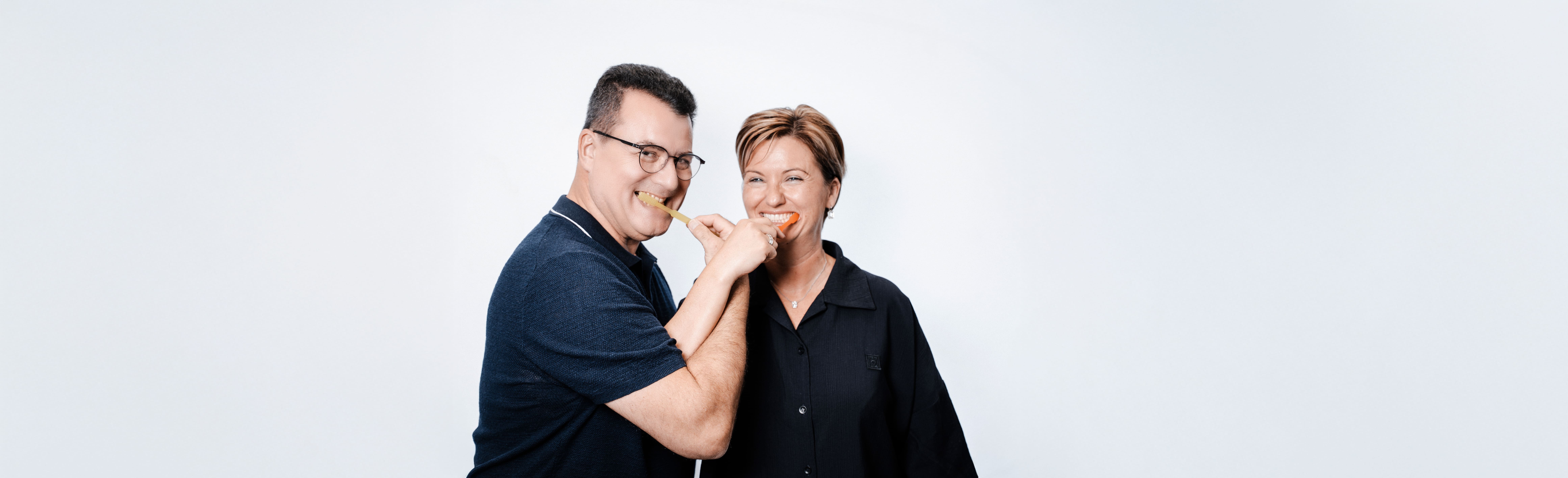 Mann und Frau lächeln, halten orange Scheiben vor Mund; blauer und schwarzer Oberkörper.