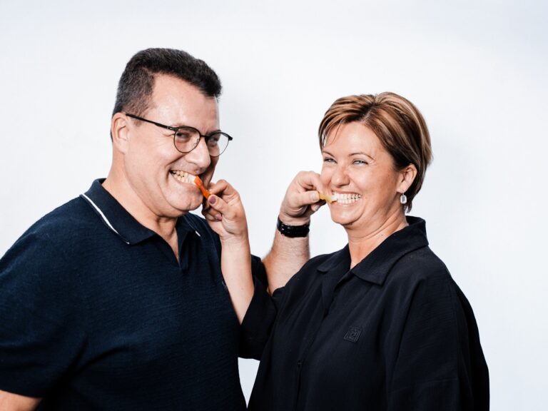 Ein Mann und eine Frau lachen und putzen sich gegenseitig die Zähne mit Zahnbürsten.