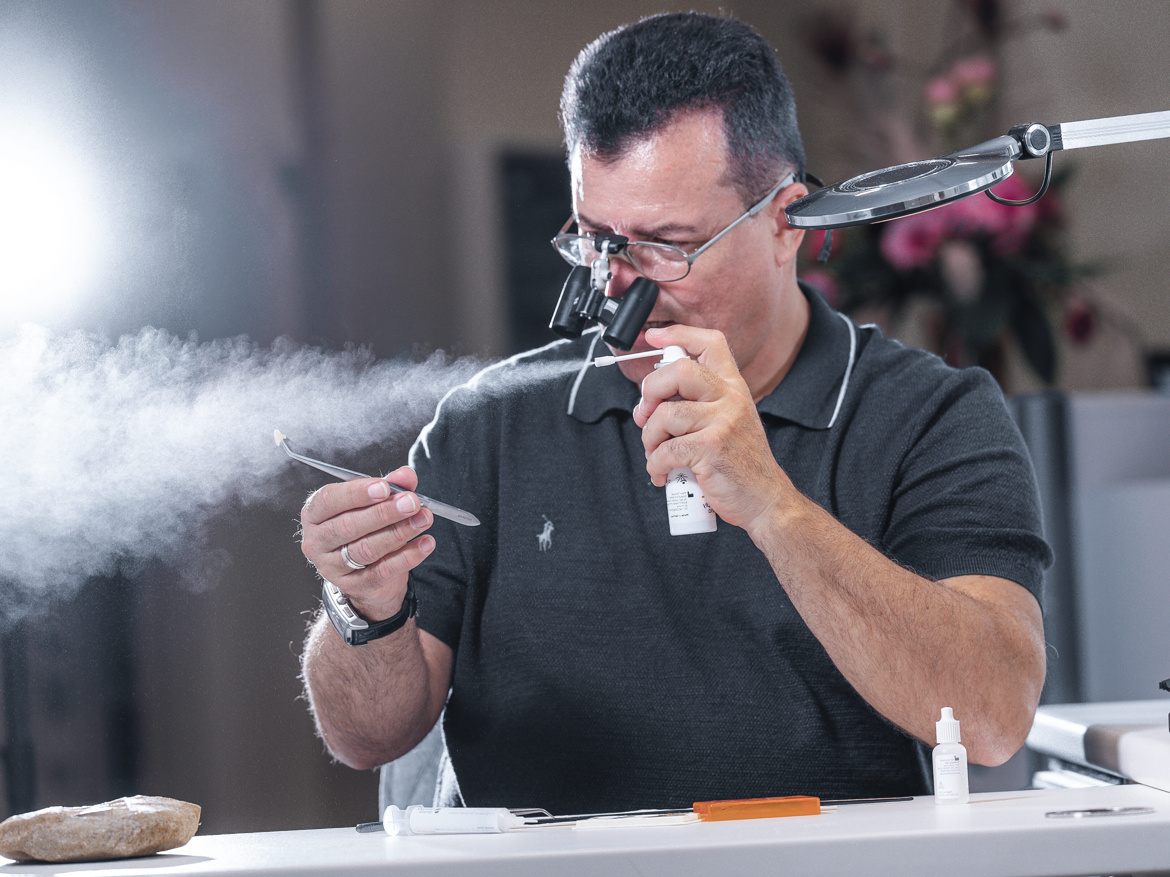 Ein Mann mit Brille und Lupe, sprüht ein Objekt an, konzentrierter Ausdruck, Polohemd.