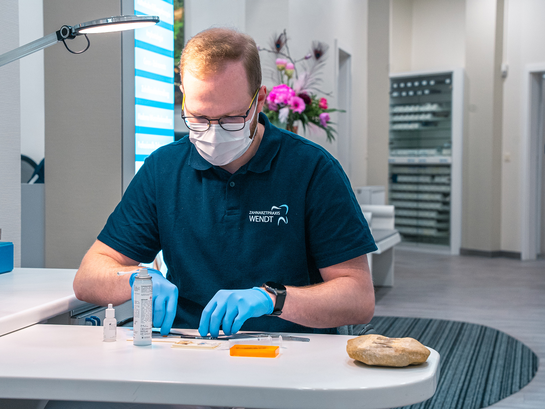 Ein Zahntechniker mit Maske arbeitet konzentriert an einem Zahnersatz, umgeben von Zahnarztwerkzeug.