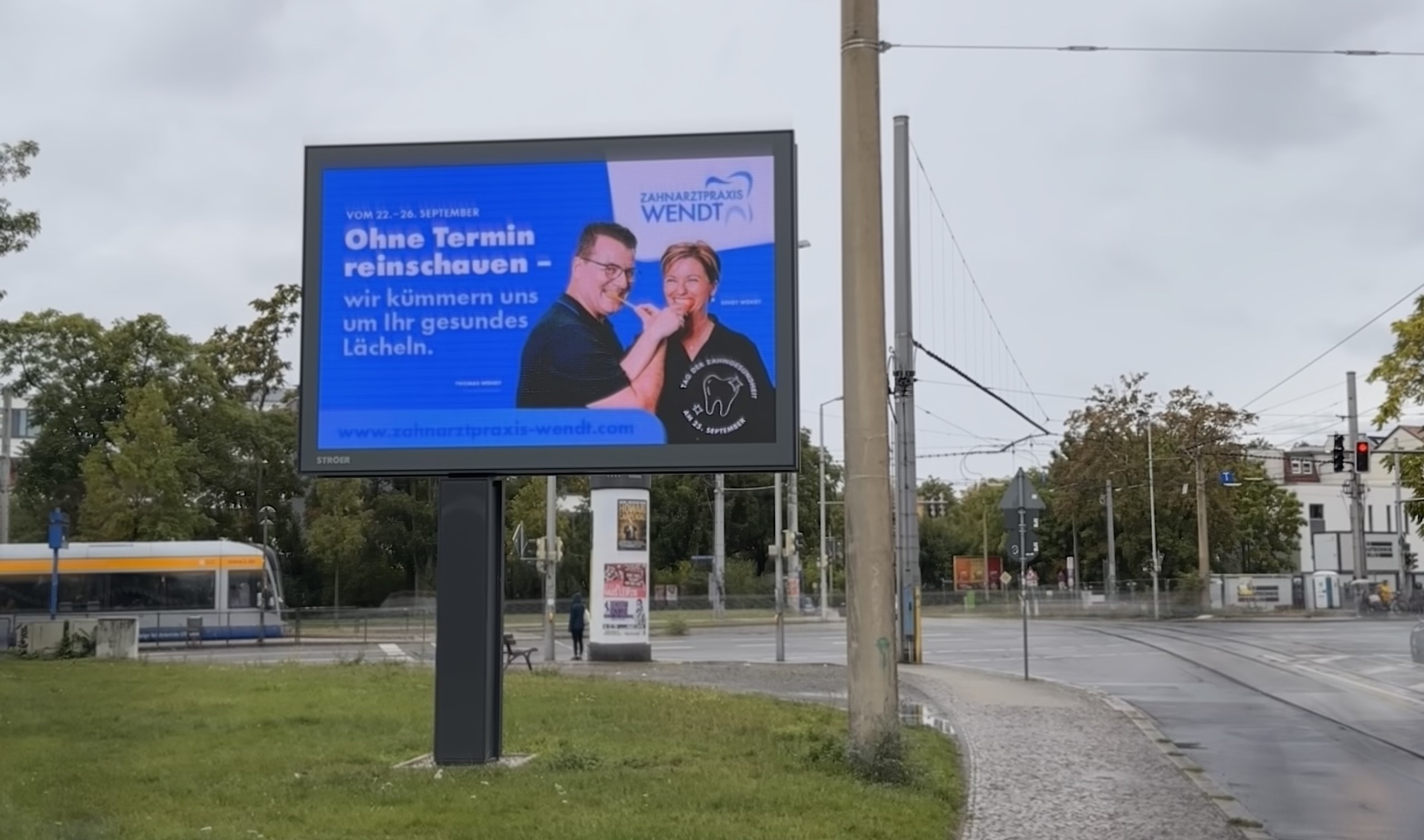 Ein Mann und eine Frau lächeln freundlich auf einem blauen Werbeplakat an einer Straßenecke