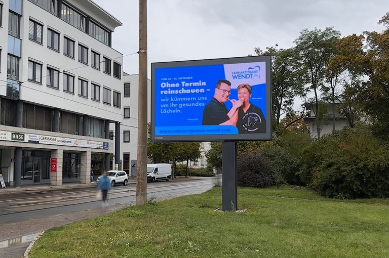 Zwei freundlich lachende Personen vor blauem Hintergrund mit weißem Werbetext