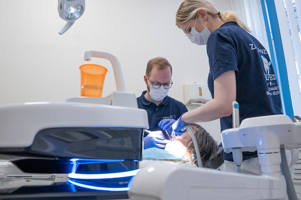 Zwei Zahnärzte mit Masken behandeln eine Patientin konzentriert in einer hellen Praxis