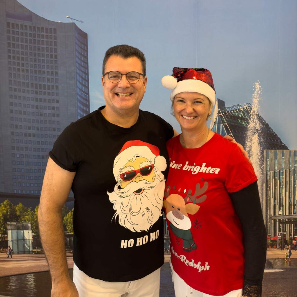 Zwei lächelnde Erwachsene stehen nebeneinander vor Stadtmotiv, festlich gekleidet